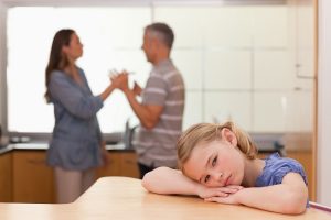 Sad girl hearing her parents arguing in a kitchen