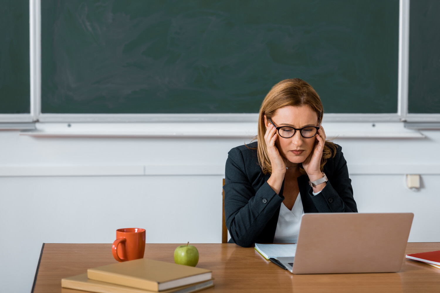 female teacher sitting at computer desk and having headache in class