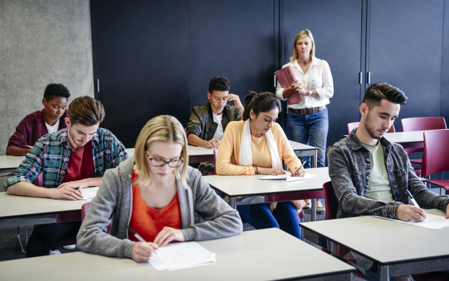 Group of college students in exam, teacher watching