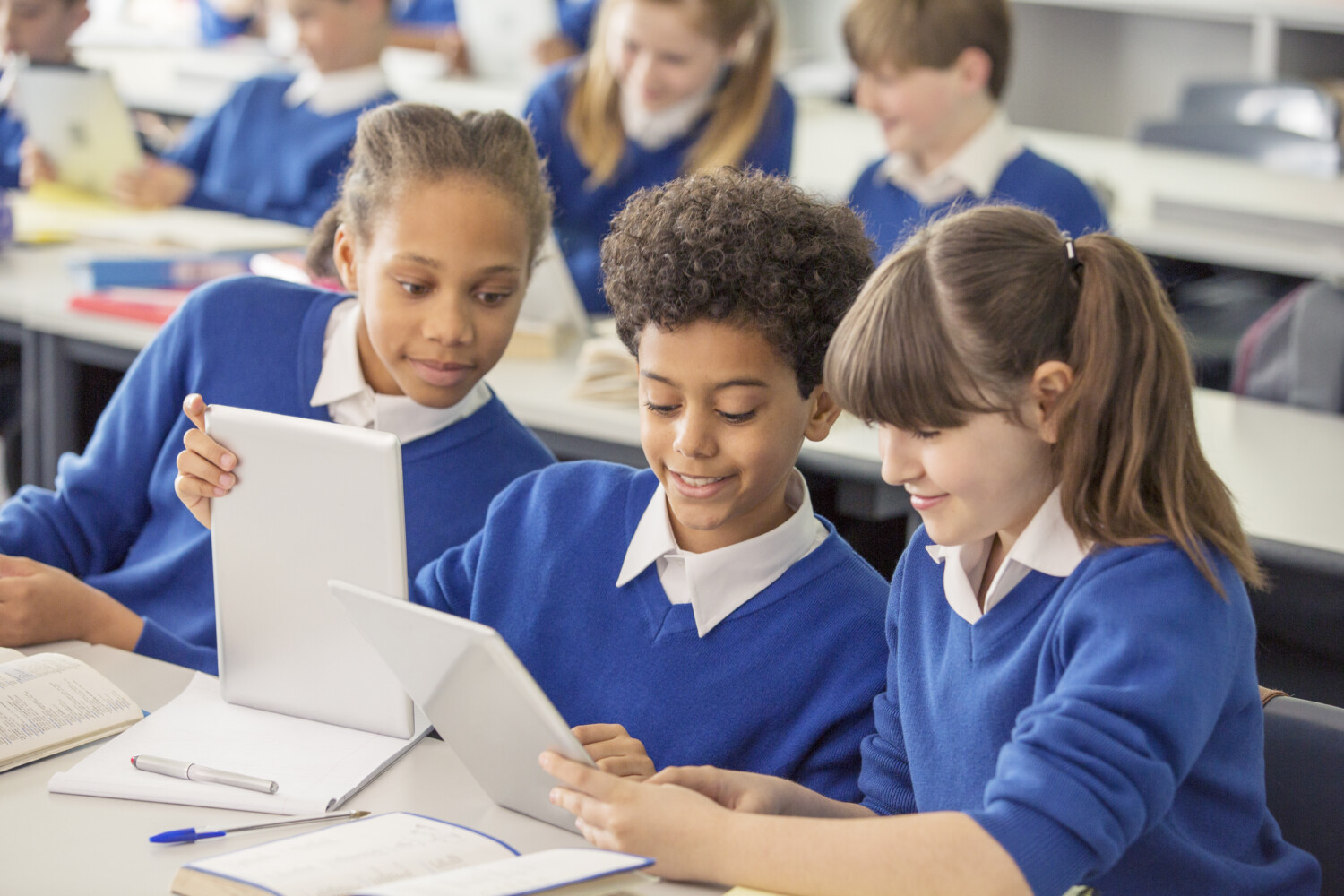 Uniforme à l’école : le ministère redéploie des crédits pour financer la poursuite de l’expérimentation Elementary school children wearing blue school uniforms using digital tablets at desk in classroom