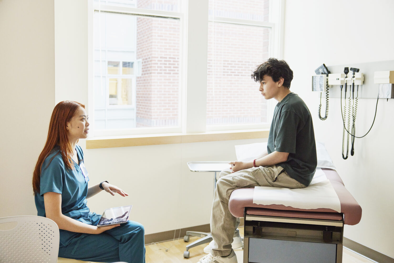 Medium wide shot  nurse consulting with teen boy in medical exam room
