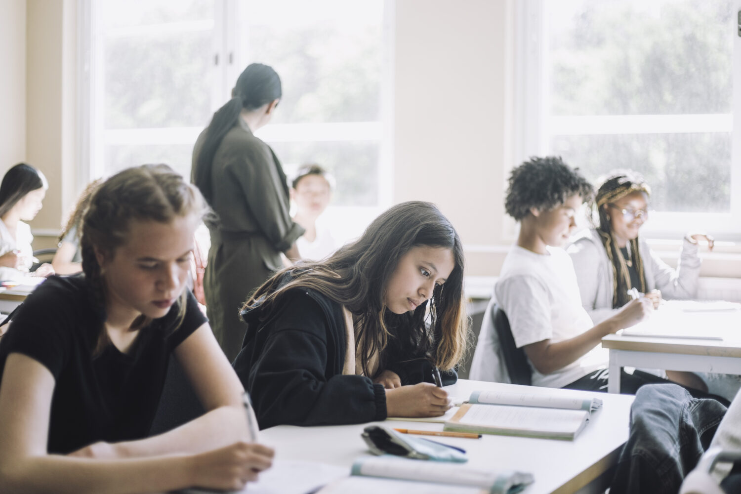 Teenage girls writing in book on desk during at junior high school