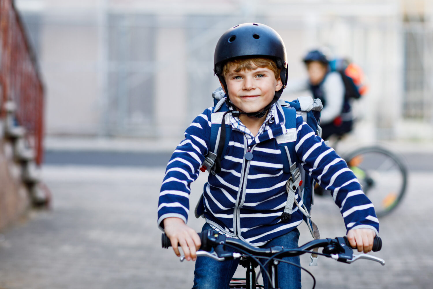 "P’tit tour" : une initiative de l’USEP pour faire pédaler et marcher les enfants Two school kid boys in safety helmet riding with bike in the city with backpacks. Happy children in colorful clothes biking on bicycles on way to school. Safe way for kids outdoors to school