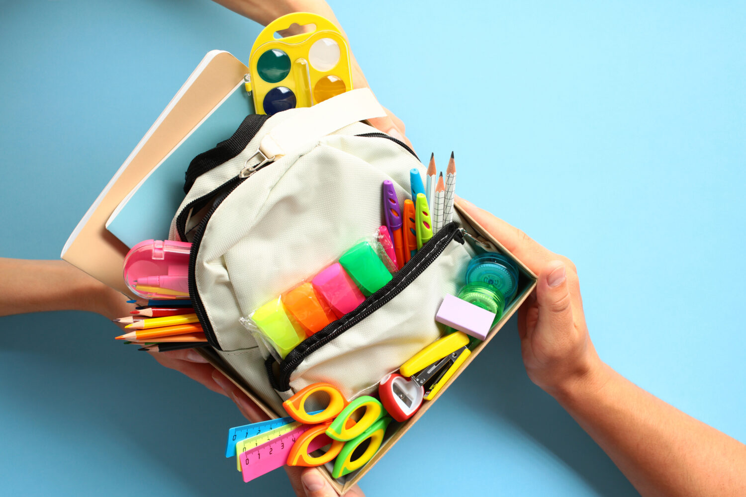 Rentrée 2025 : les fournitures scolaires gratuites dans plusieurs grandes villes Back to school donation drive concept. Top view cardboard box with backpack full of colorful school supplies.